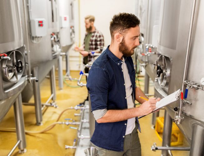 manufacture, business and people concept - men with clipboard working at craft brewery or beer plant
